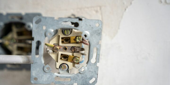 Electrical socket opened up in a plaster wall, showing colour-coded wiring and terminal screws