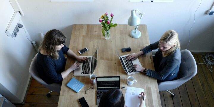 Three women sitting around a table using laptops in a working session