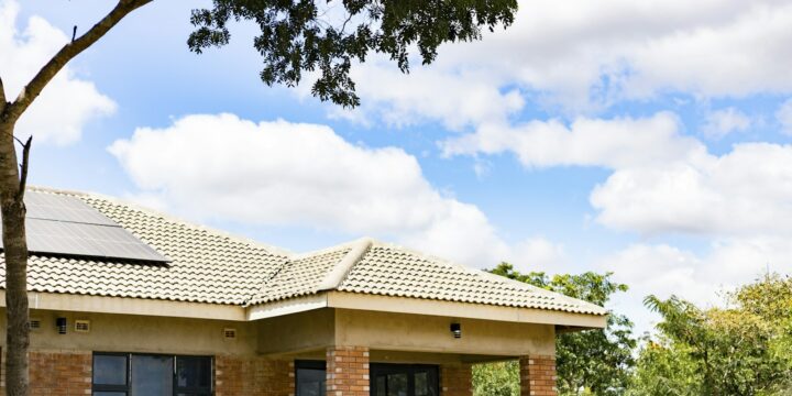 Brick house with a veranda and solar panels on its tiled roof under a blue sky